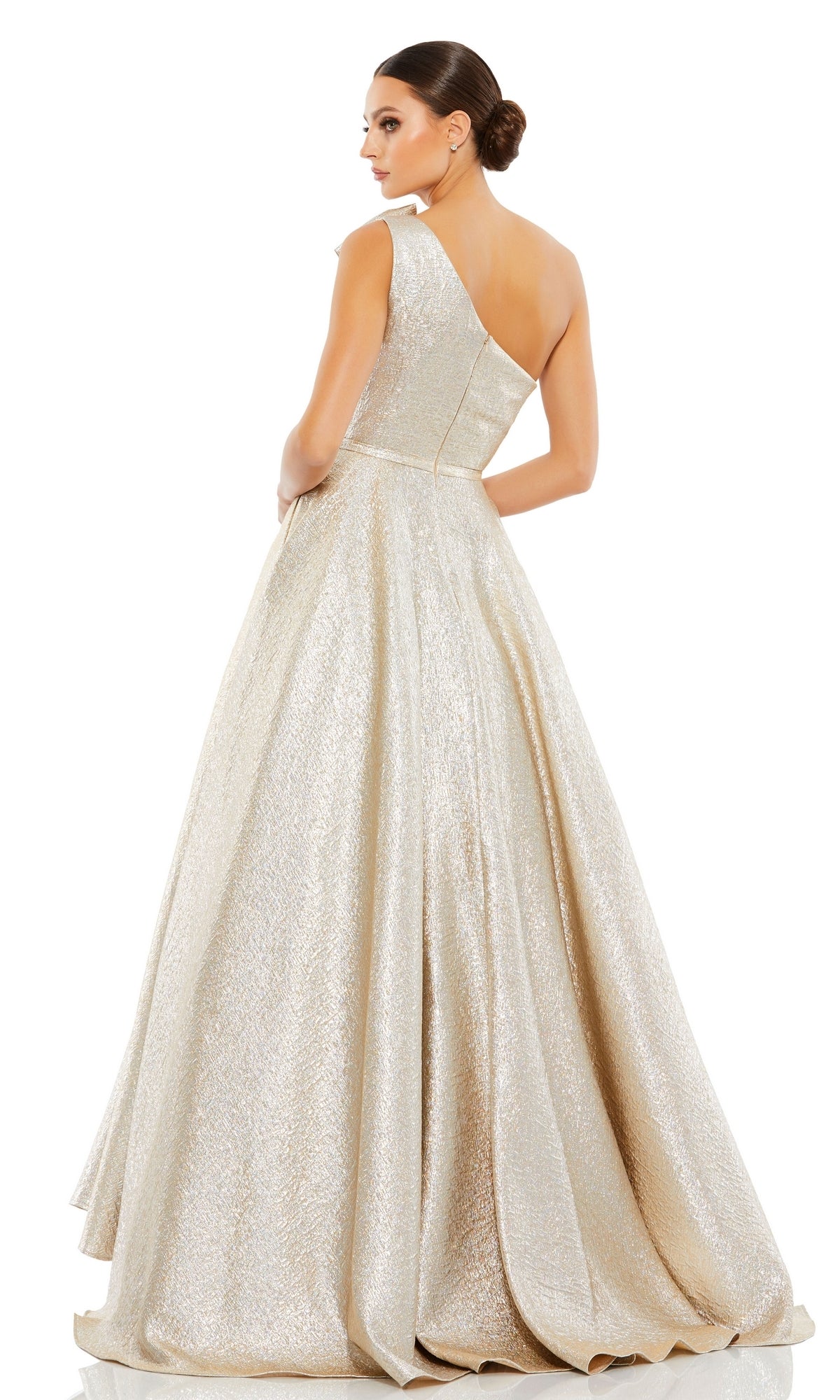 A woman in the Long Formal Dress 67890 by Mac Duggal, a shimmering floor-length one-shoulder metallic gown, stands facing away and glances over her shoulder with her hair in a low bun.